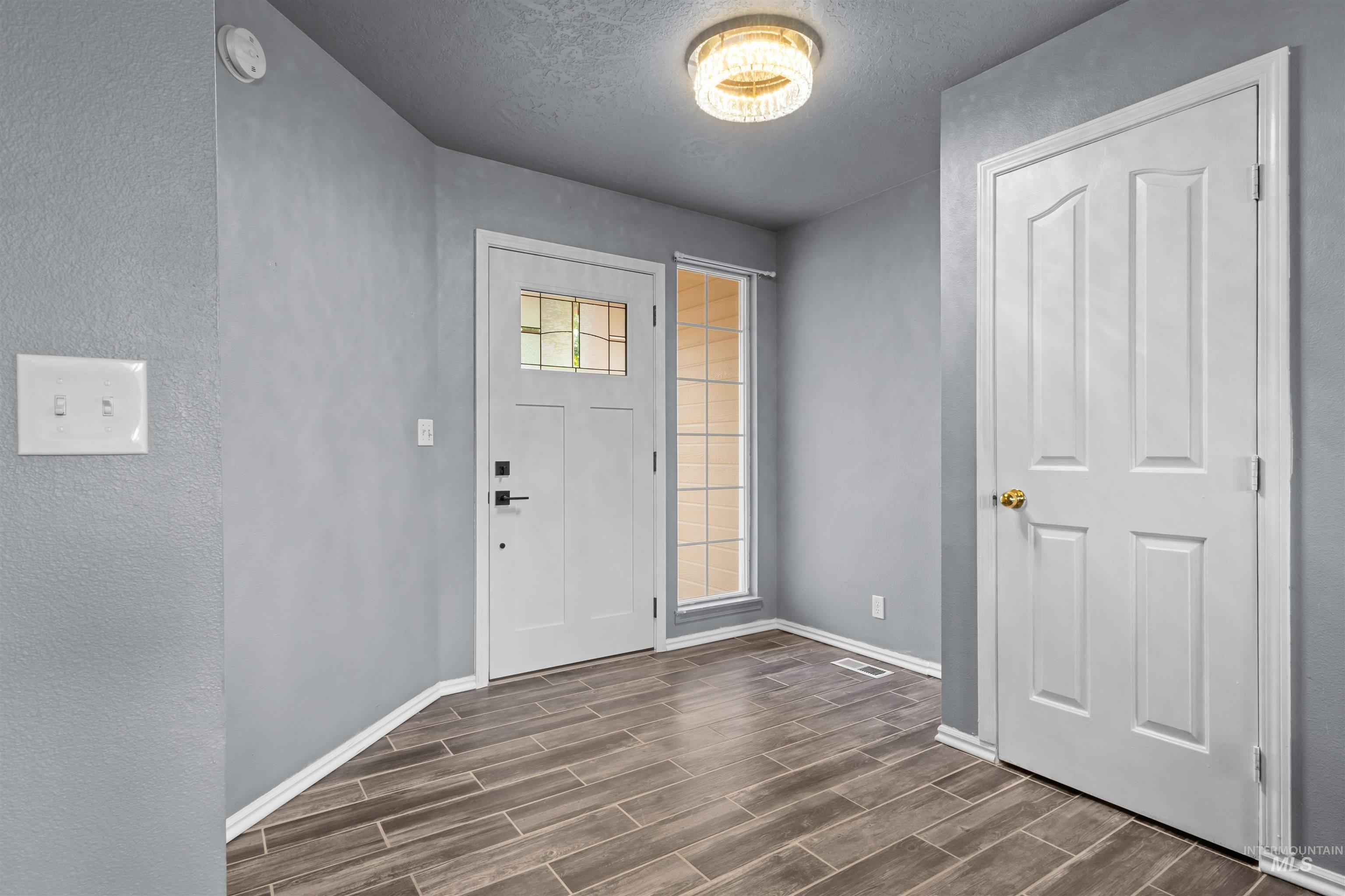 Entry foyer with wood-look tile floors, a white glass-panel front door, and a tall sidelight window.