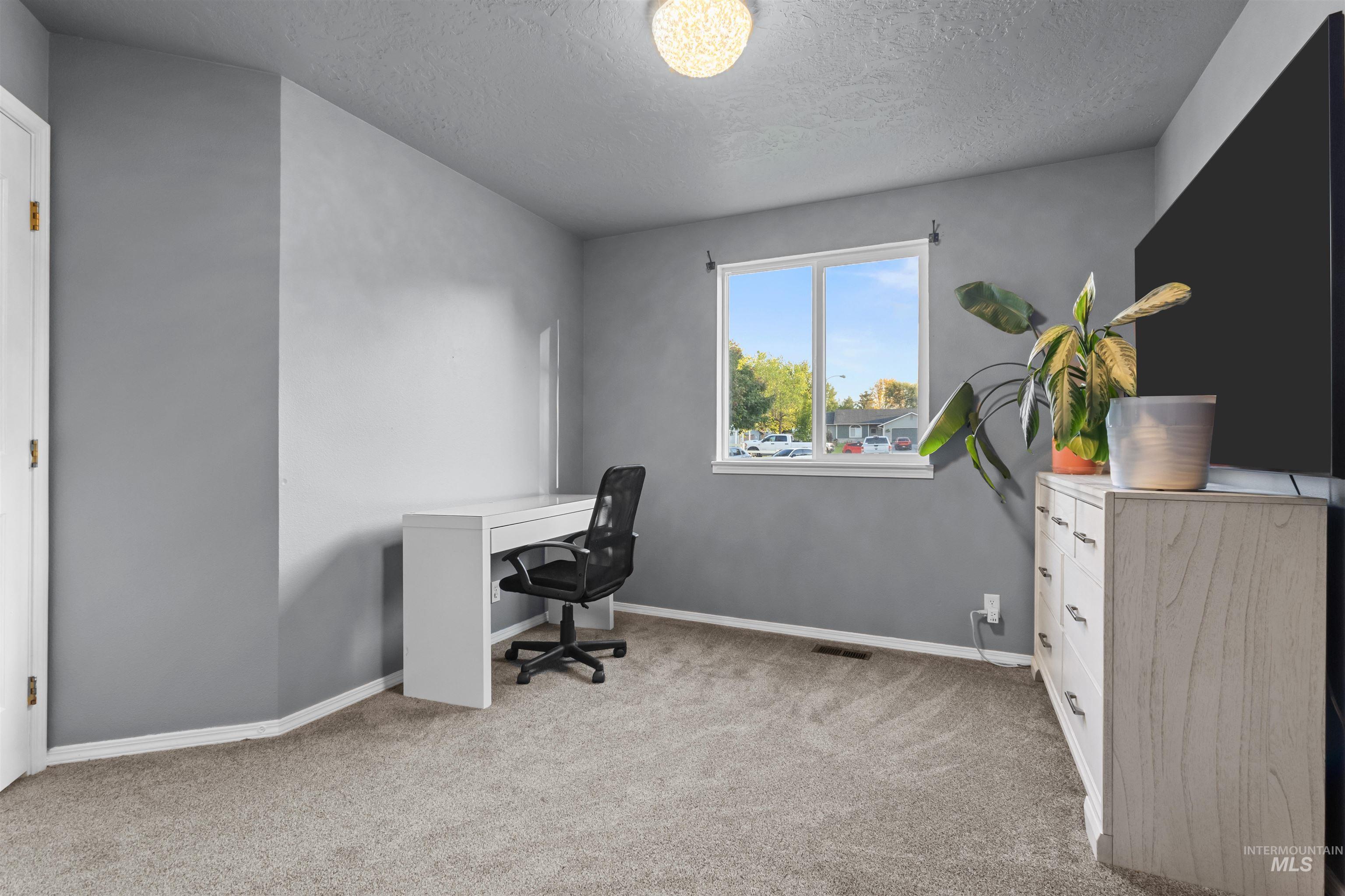 Home office with a white desk and black chair, gray walls, and a window overlooking the neighborhood.