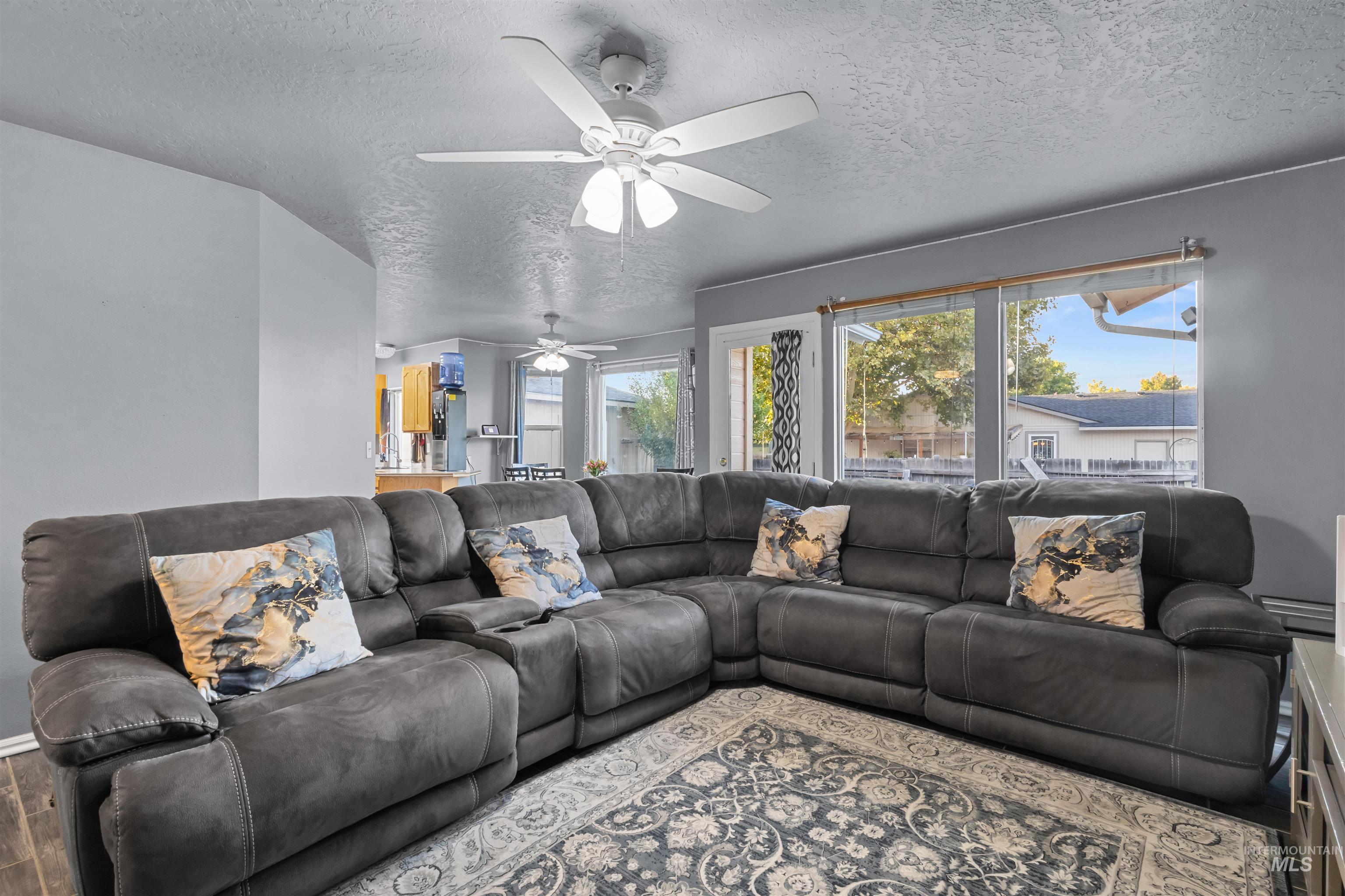 Living room with a dark gray sectional, patterned pillows, and large windows overlooking the backyard.