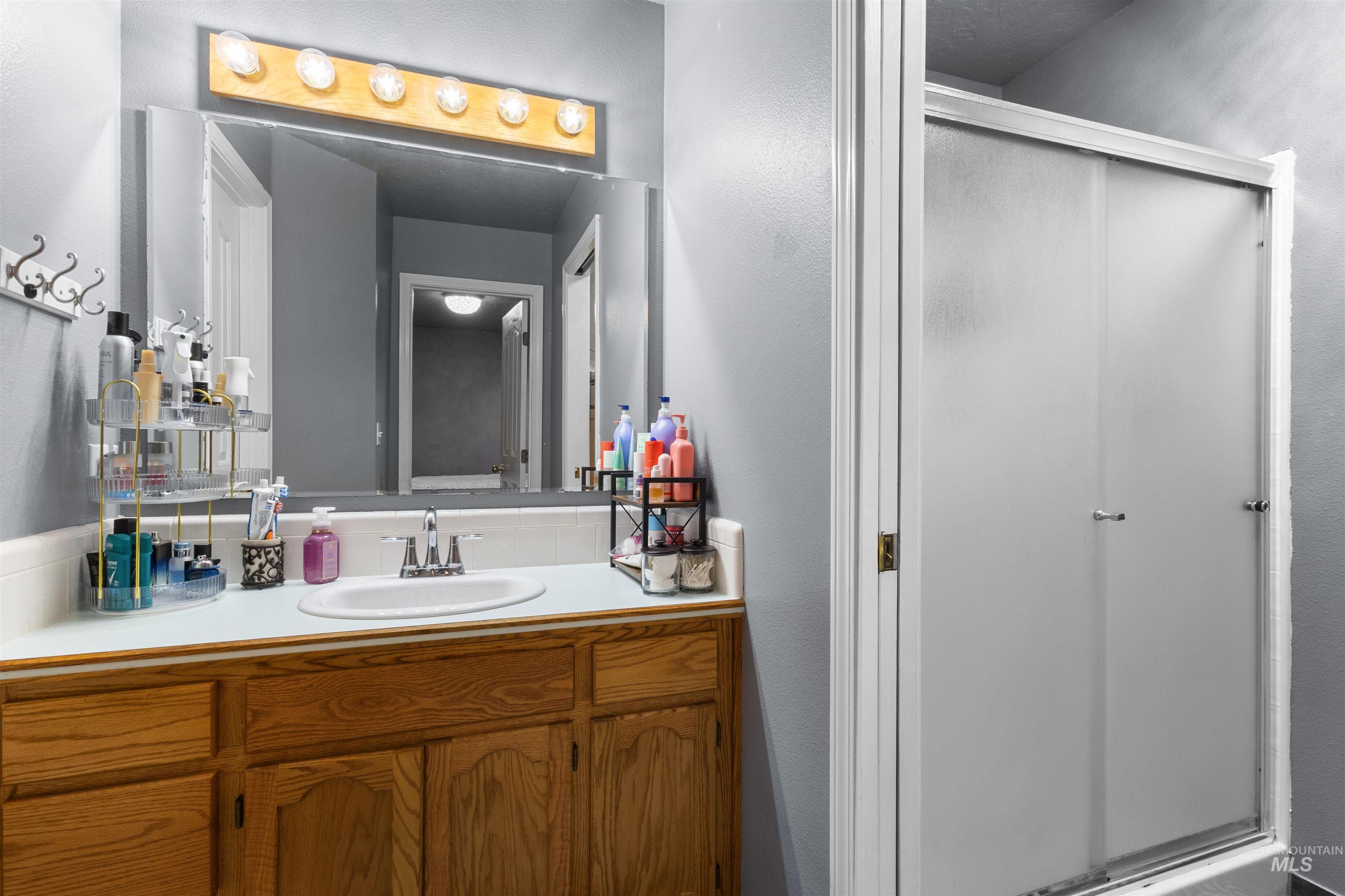 Bathroom vanity with oak cabinets, a wide mirror, and sliding shower doors.