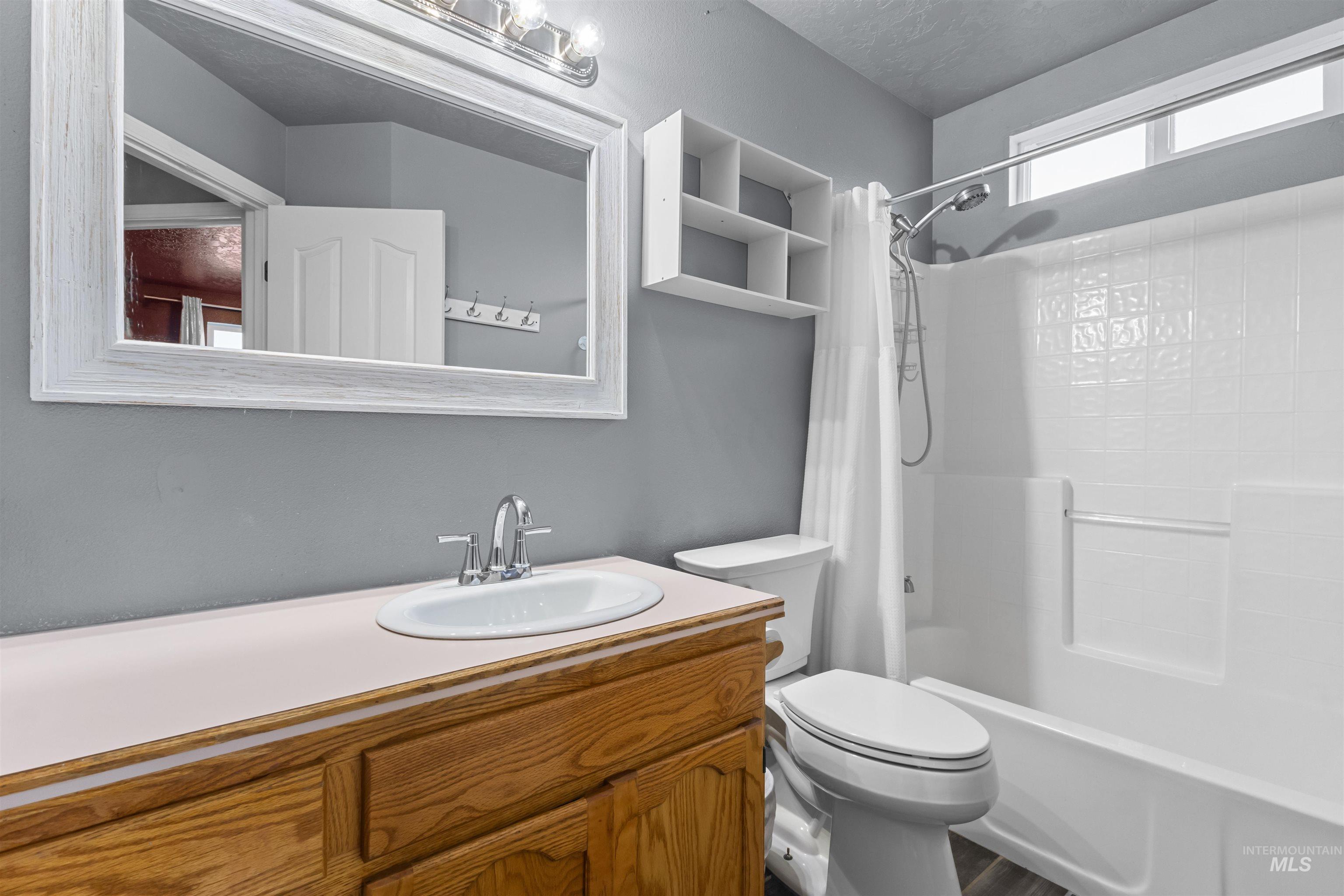 Bathroom with a wood vanity, large framed mirror, and white tub-shower combination.