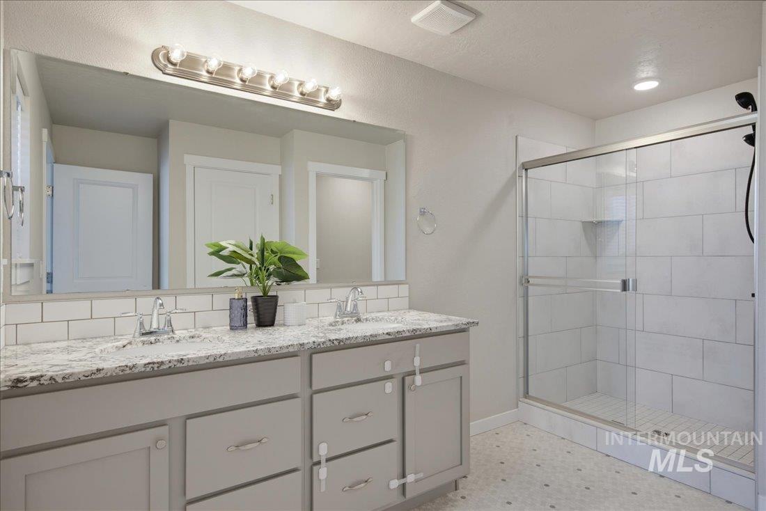 Bathroom with a long gray double-sink vanity and a glass-enclosed white-tile shower.