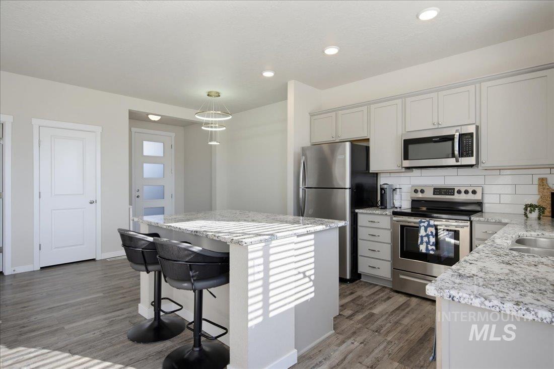 Kitchen with a granite island and stools, white cabinets, and stainless steel appliances.