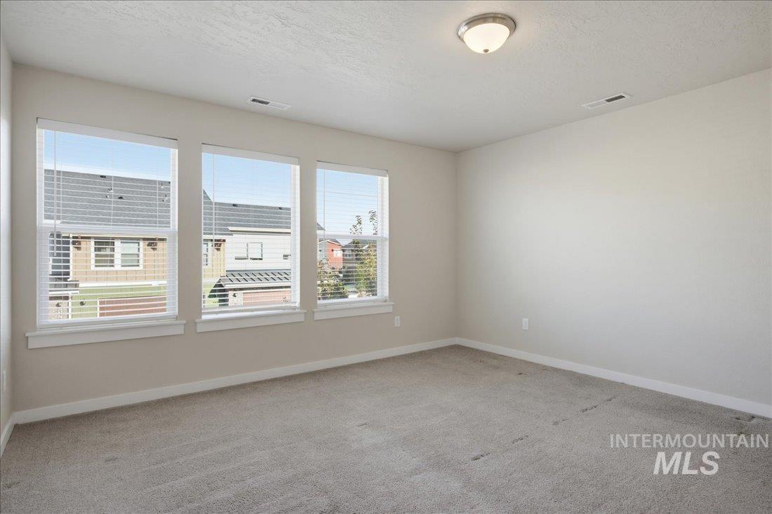 Unfurnished bedroom with light carpet and three windows overlooking neighboring homes.