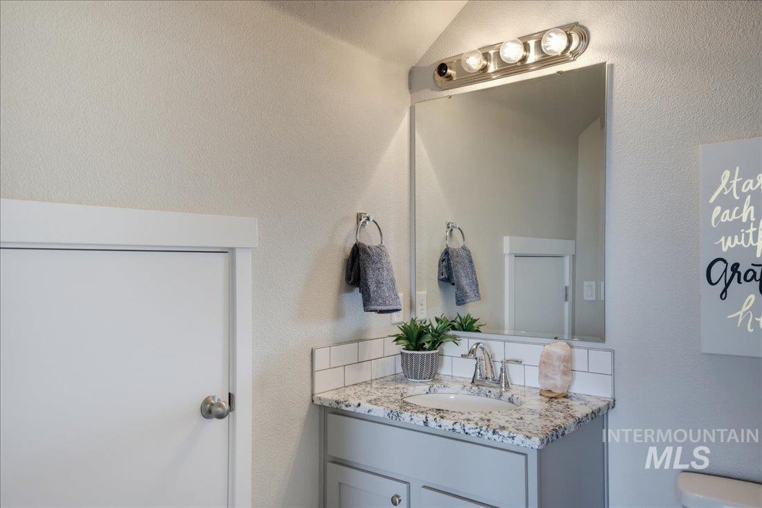 Bathroom vanity with a marbled countertop, chrome faucet, large mirror, and potted plant.