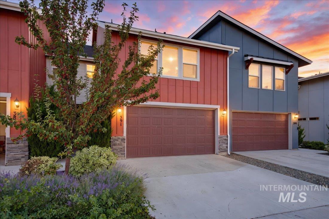 Two-story red and blue home with an attached garage, landscaped driveway, and sunset sky.