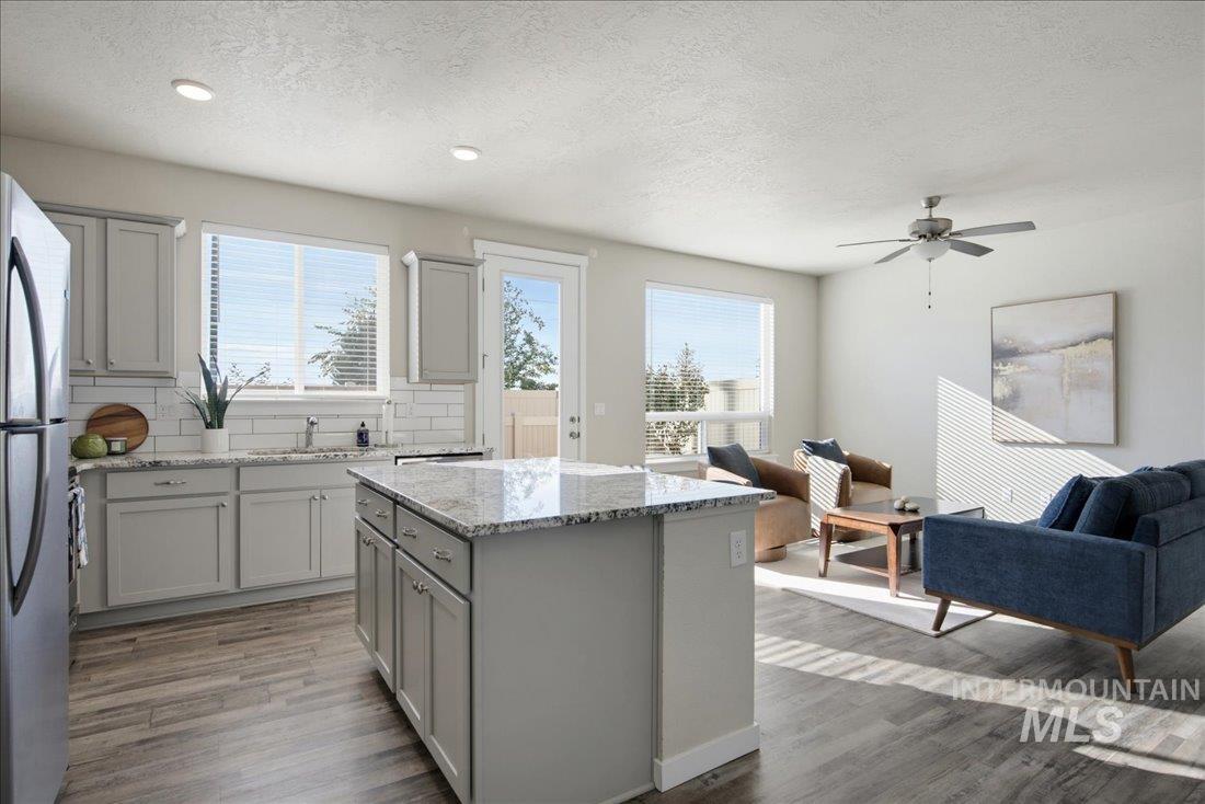 Open kitchen with a large granite island adjoining a sunlit living area.