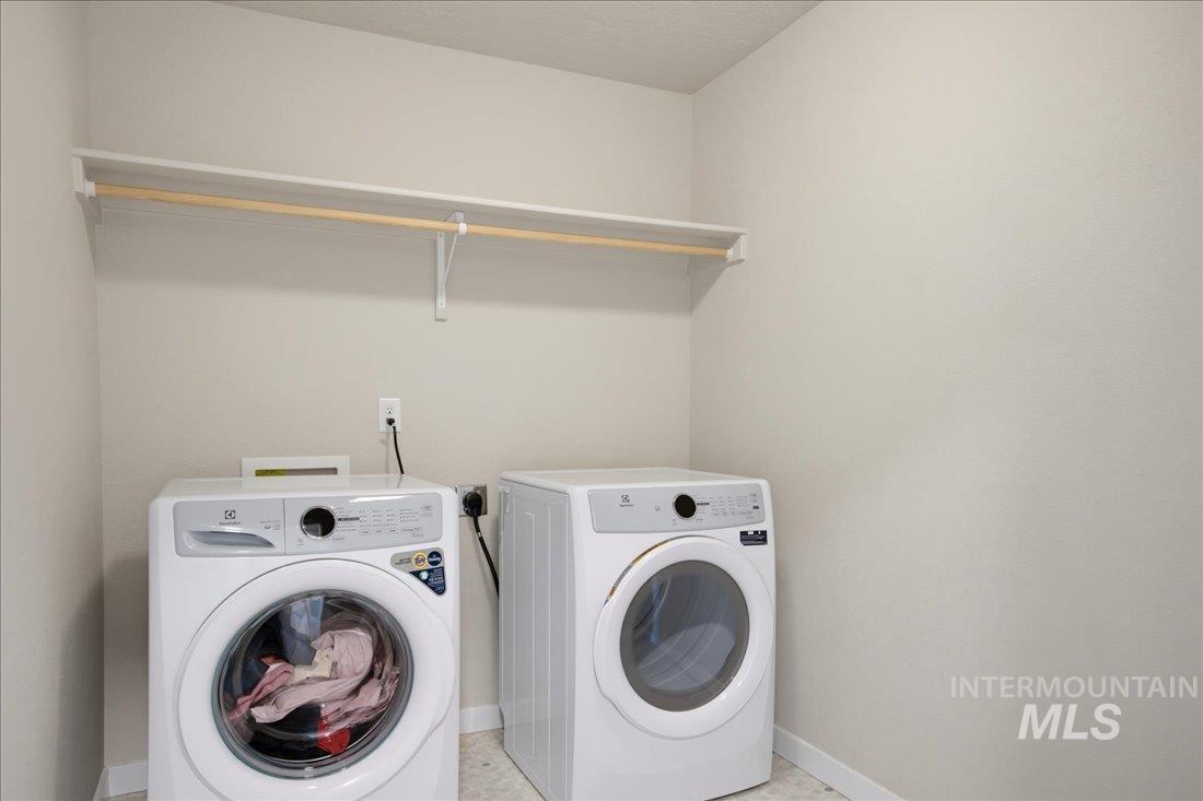 Laundry room with side-by-side front-loading washer and dryer beneath a long shelf and hanging rod.