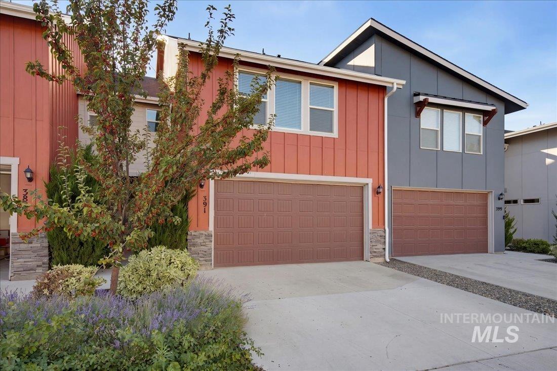 Two-story coral-red and gray home with a garage, stone accents, and flowering landscaping.