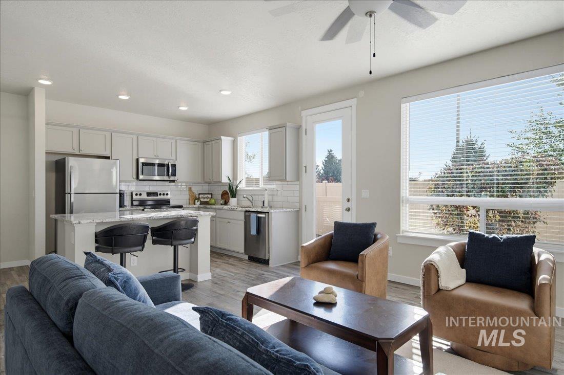 Open-plan living room and kitchen with a white-cabinet kitchen, blue sofa, and tan armchairs.