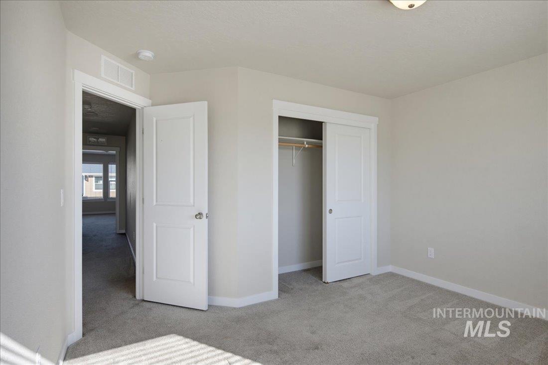 Empty carpeted bedroom with an open closet and doorway to an adjoining room.