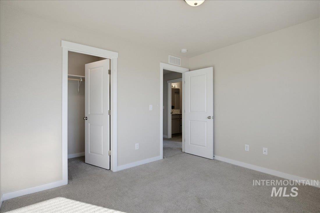 Vacant carpeted bedroom with an open closet and doorway to a bathroom.