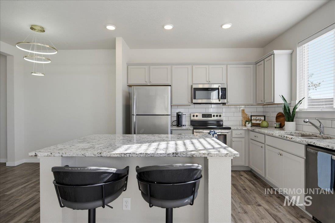 Kitchen with a granite island, two black stools, white cabinets, and stainless steel appliances.
