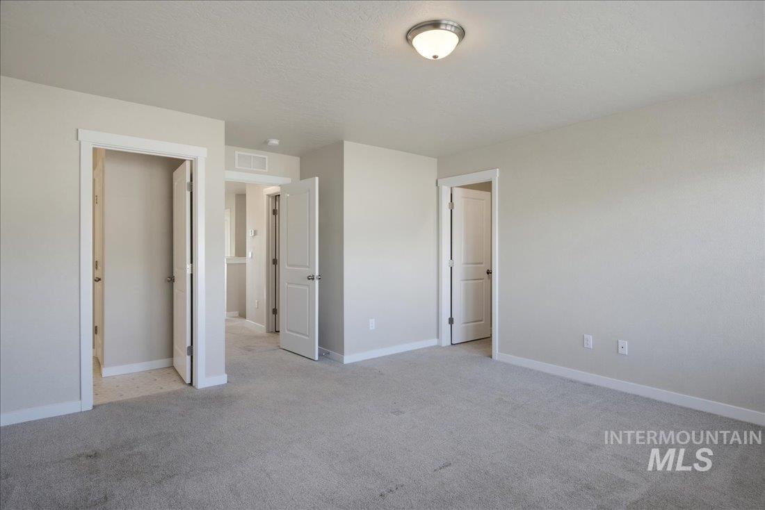 Empty carpeted bedroom with neutral walls, white trim, and several open doorways.