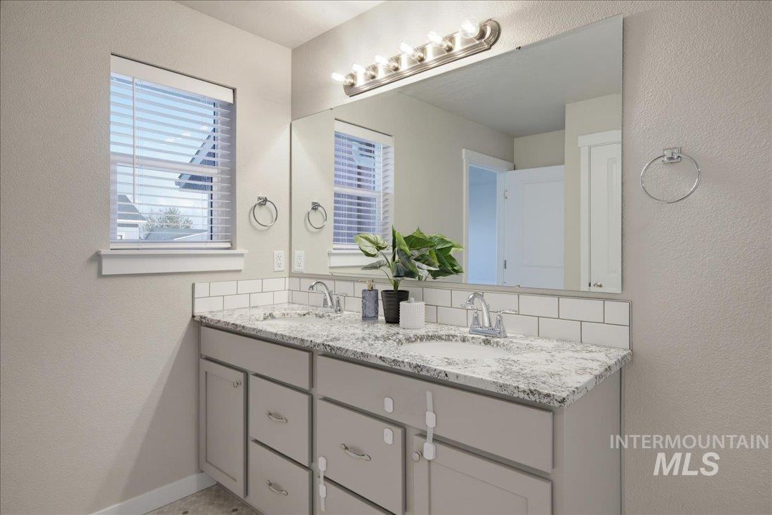 Bathroom vanity with two sinks, a speckled stone countertop, and a large mirror.