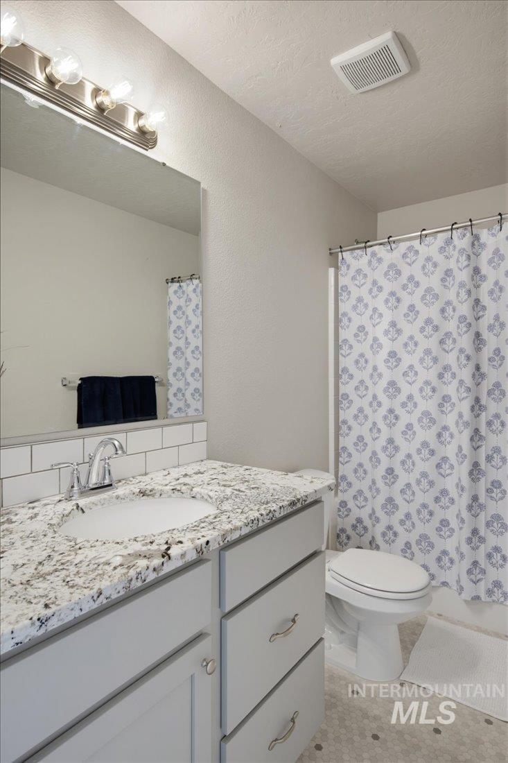 Bathroom with a granite vanity and purple floral shower curtain.