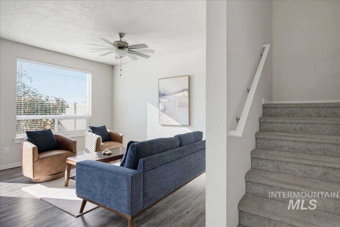 Staged living room with blue sofa and brown armchairs beside a carpeted staircase.