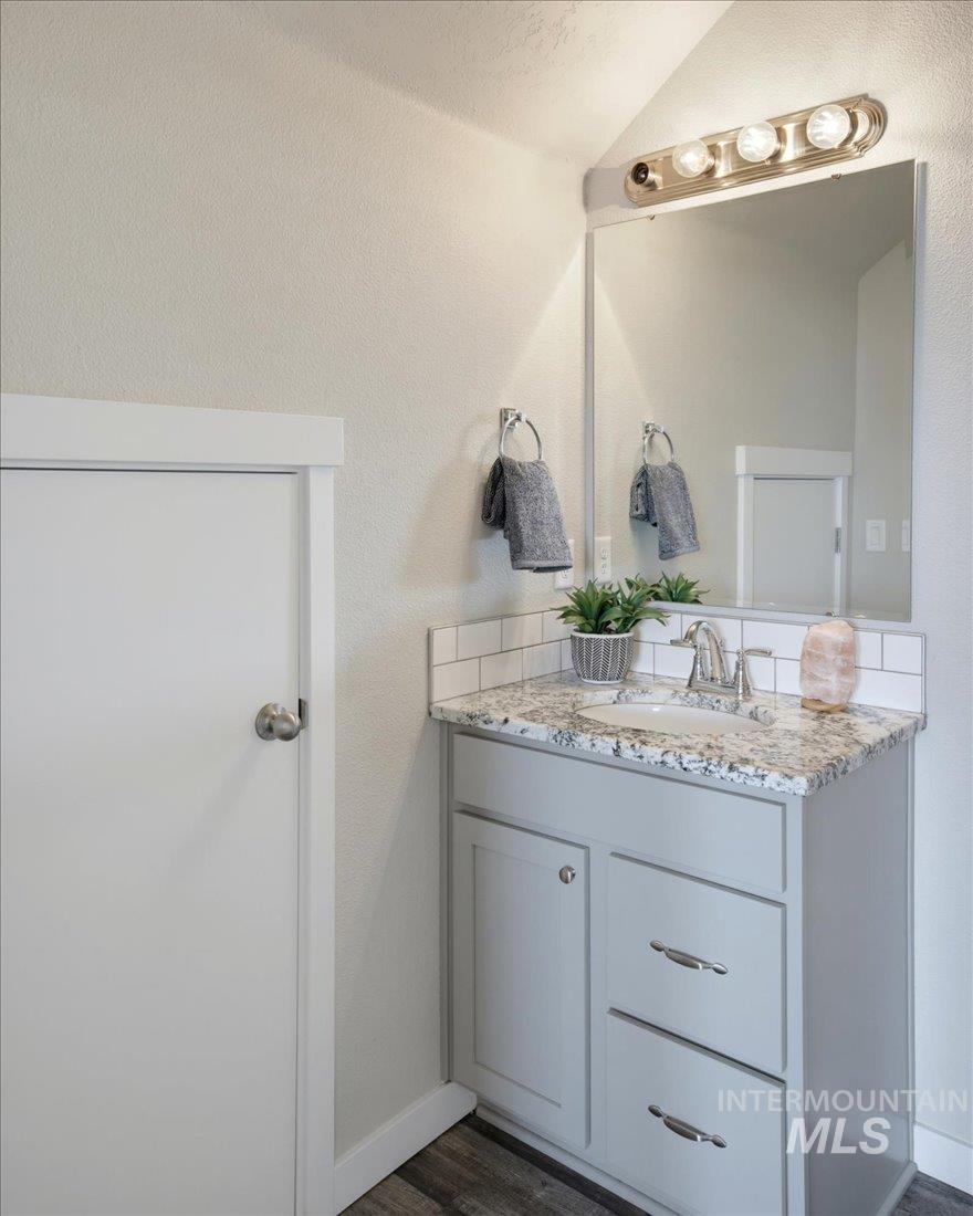 Bathroom vanity with a speckled stone countertop, gray cabinetry, and a large mirror.