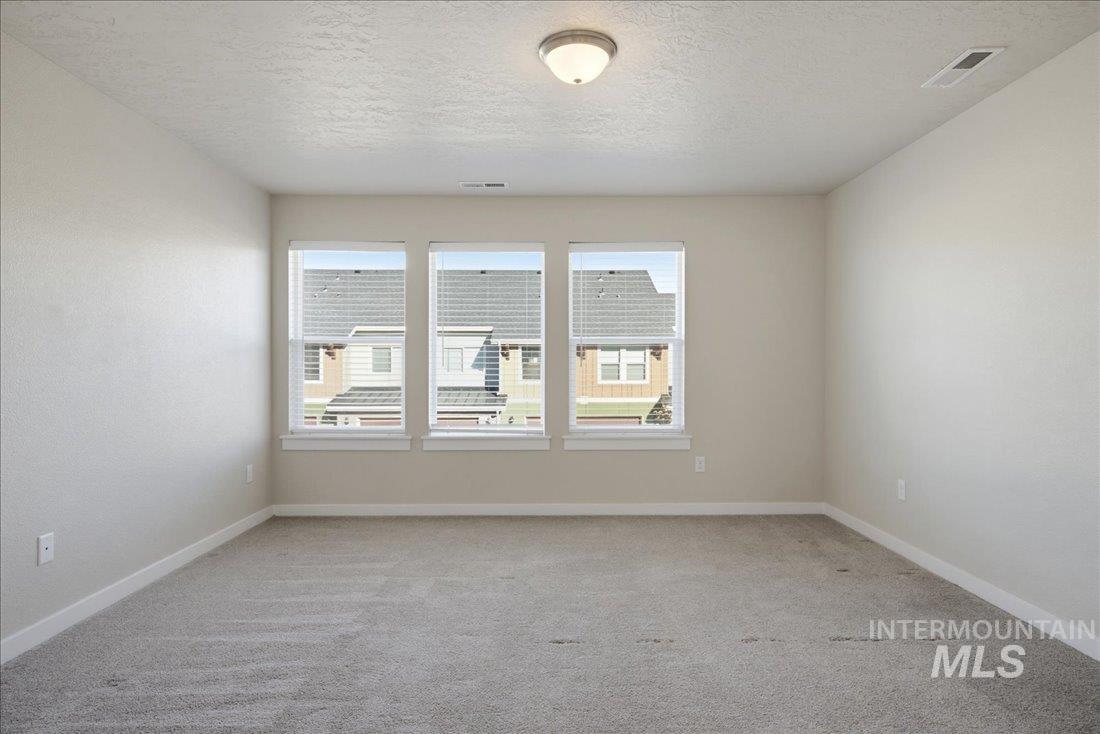 Empty carpeted bedroom with three windows and a ceiling light.
