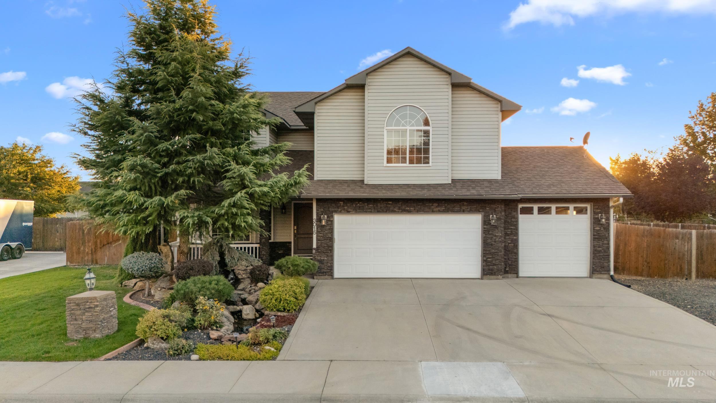 Two-story home with stone facade, arched upper window, landscaped yard, and three-car garage.