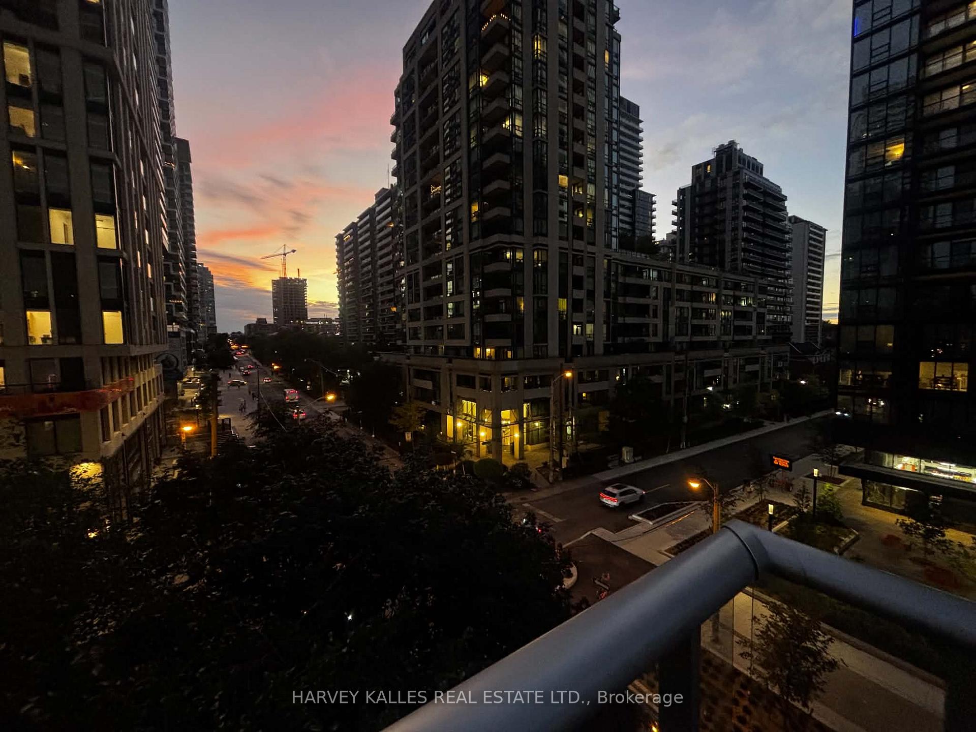 Condominium towers and city streets at dusk, viewed over a balcony railing.