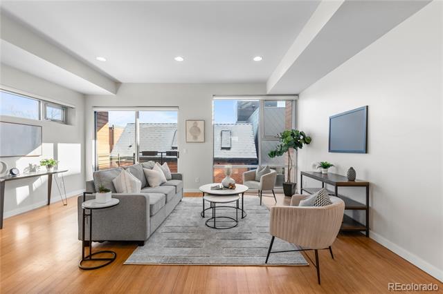 Staged living room with a gray sofa, accent chairs, hardwood floors, and large windows.