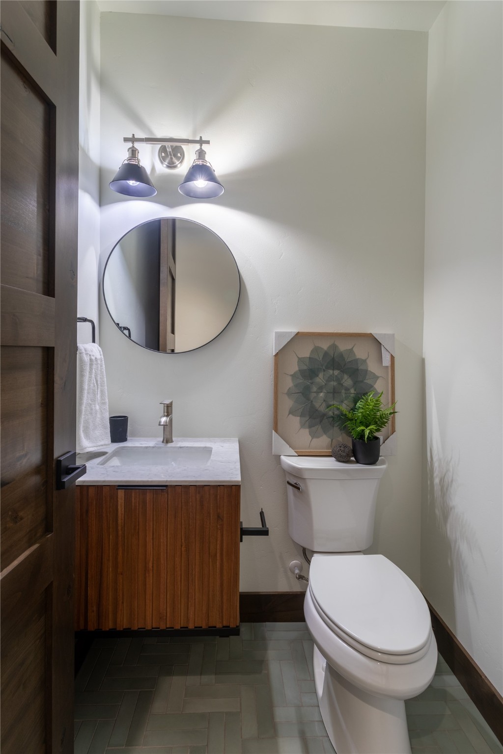 Bathroom with walnut vanity, round mirror, and botanical artwork above the toilet.