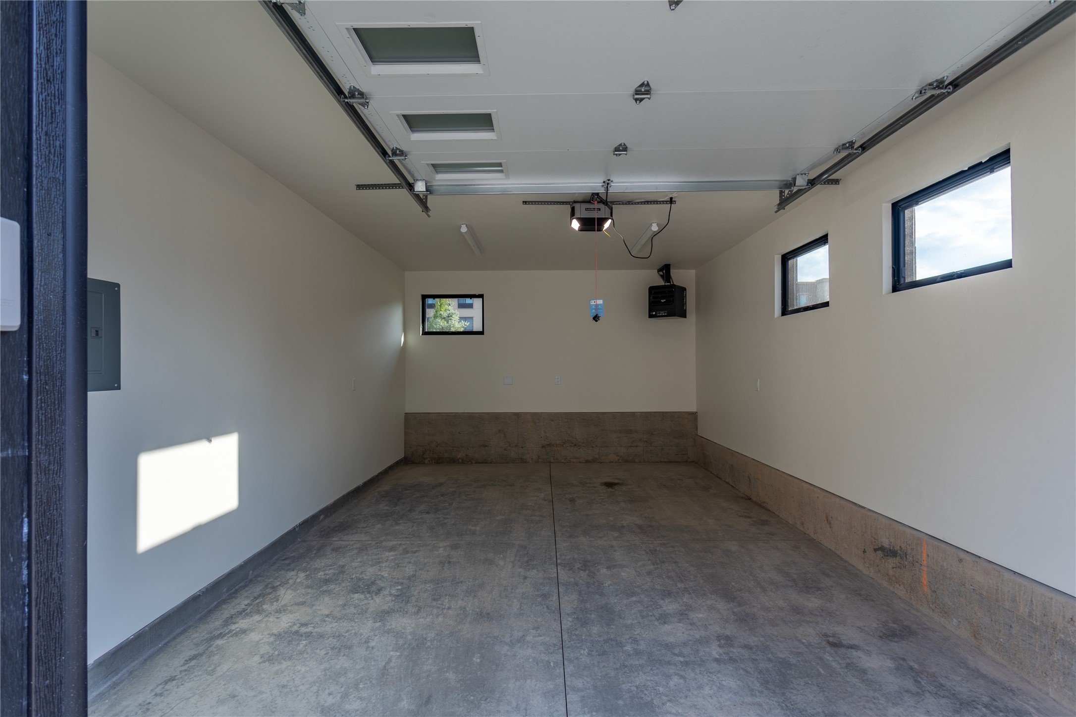 Empty garage with a concrete floor, three windows, and an open overhead door.