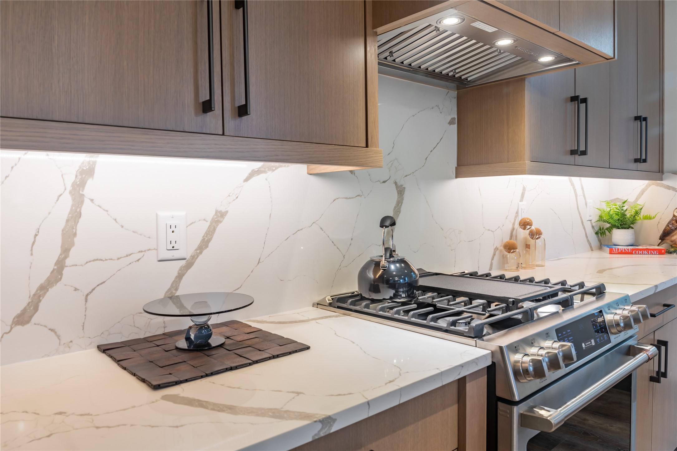 Modern kitchen with a stainless-steel gas range, wood cabinets, and white veined stone counters.