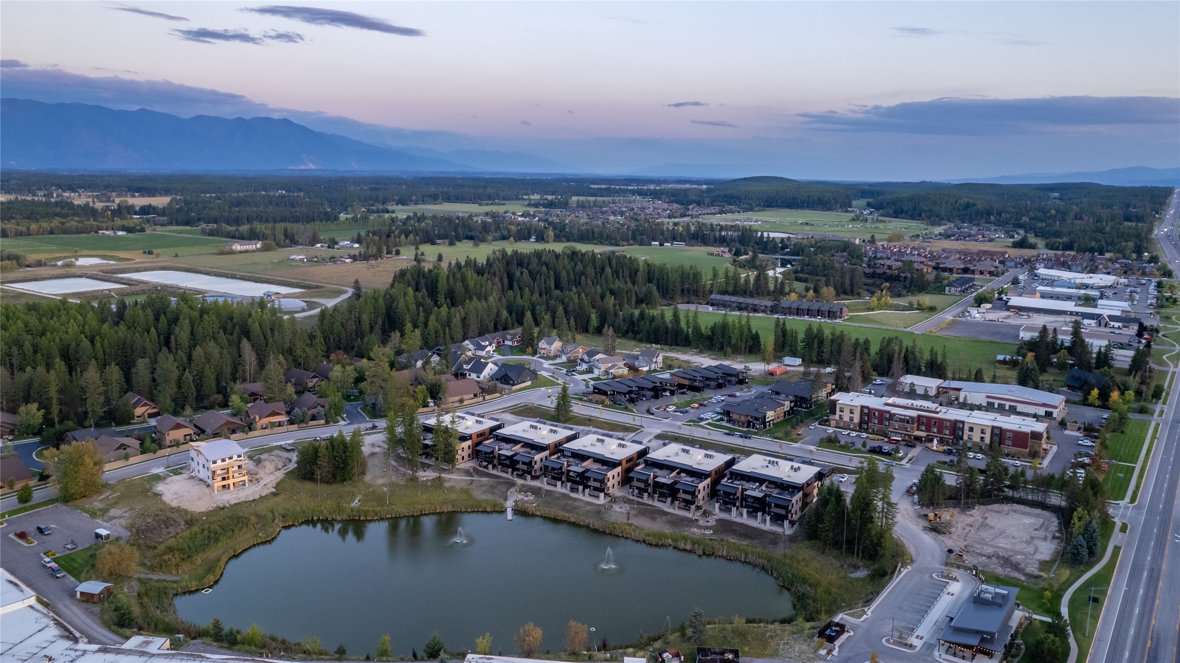 Aerial view of lakeside townhomes and apartments, with fountains in the lake and mountains beyond.