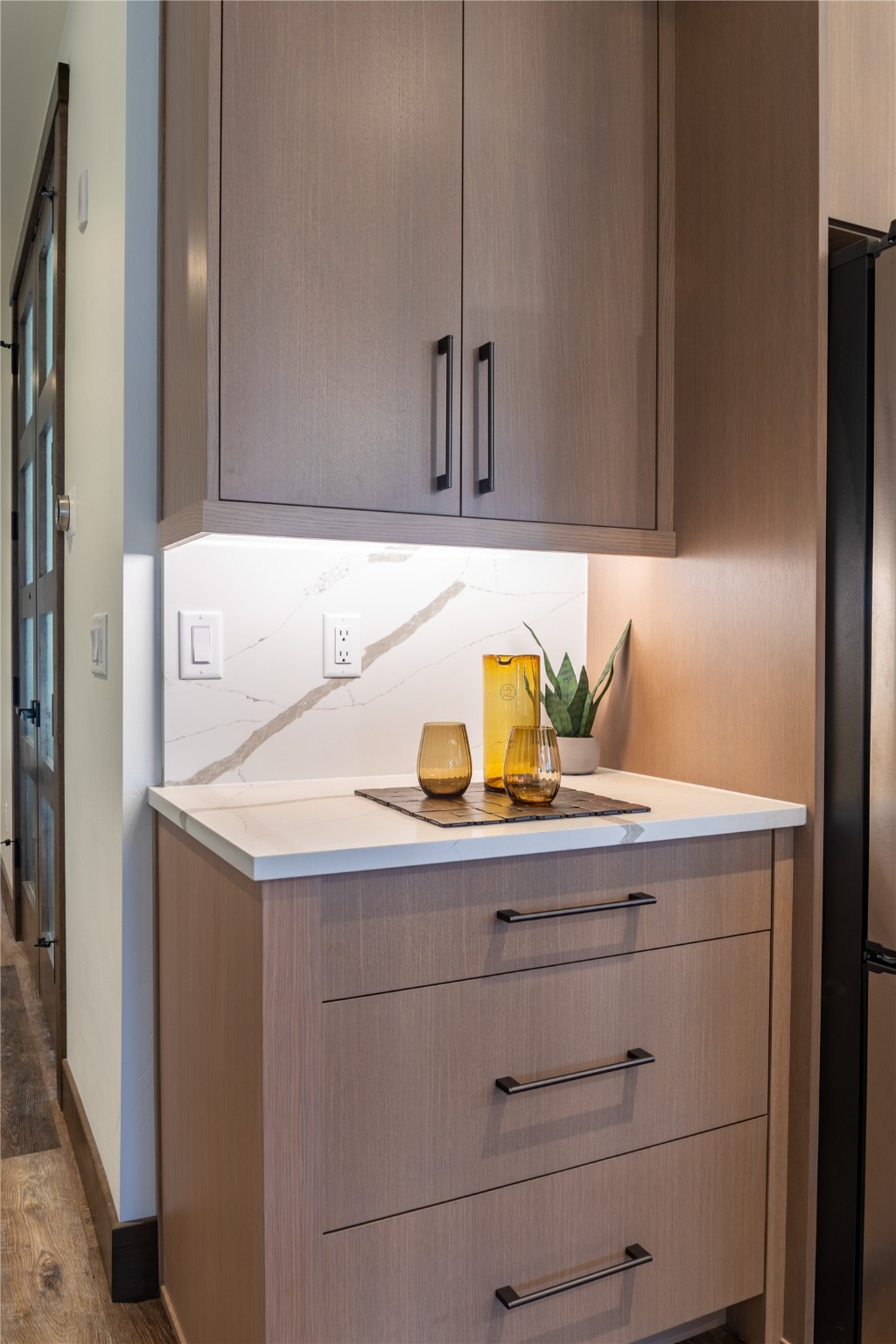 Built-in wood cabinetry with a veined stone backsplash, white counter, amber glass decor, and a small plant.