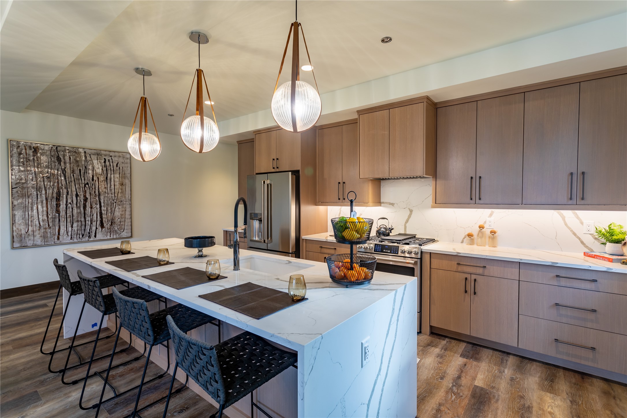 Modern kitchen with wood cabinets, a marble-look island, black bar stools, and three glass pendant lights.
