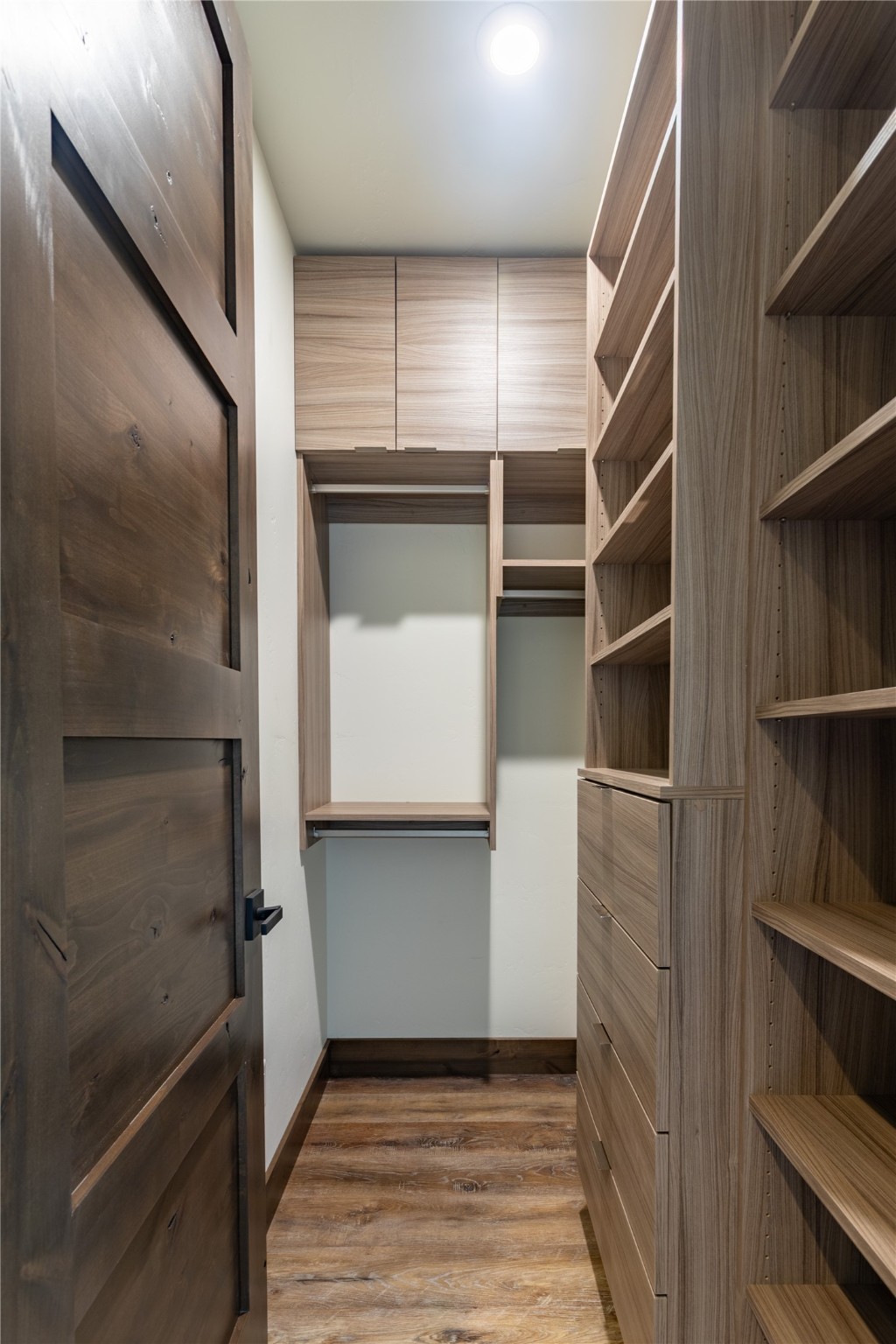 Walk-in closet with walnut-toned built-in shelving, drawers, hanging space, and wood flooring.