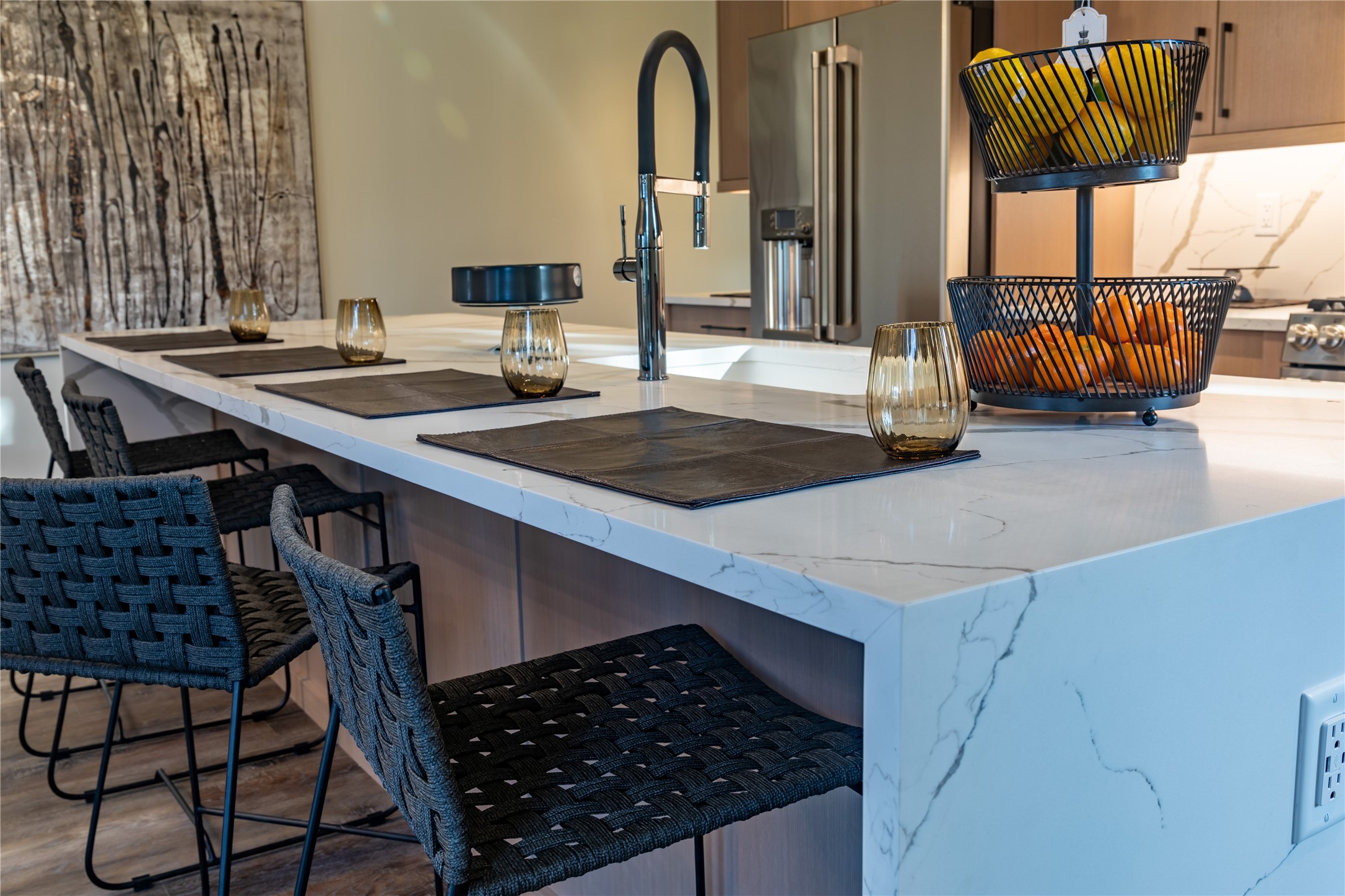 Modern kitchen with a veined stone island, woven bar chairs, and stainless steel refrigerator.