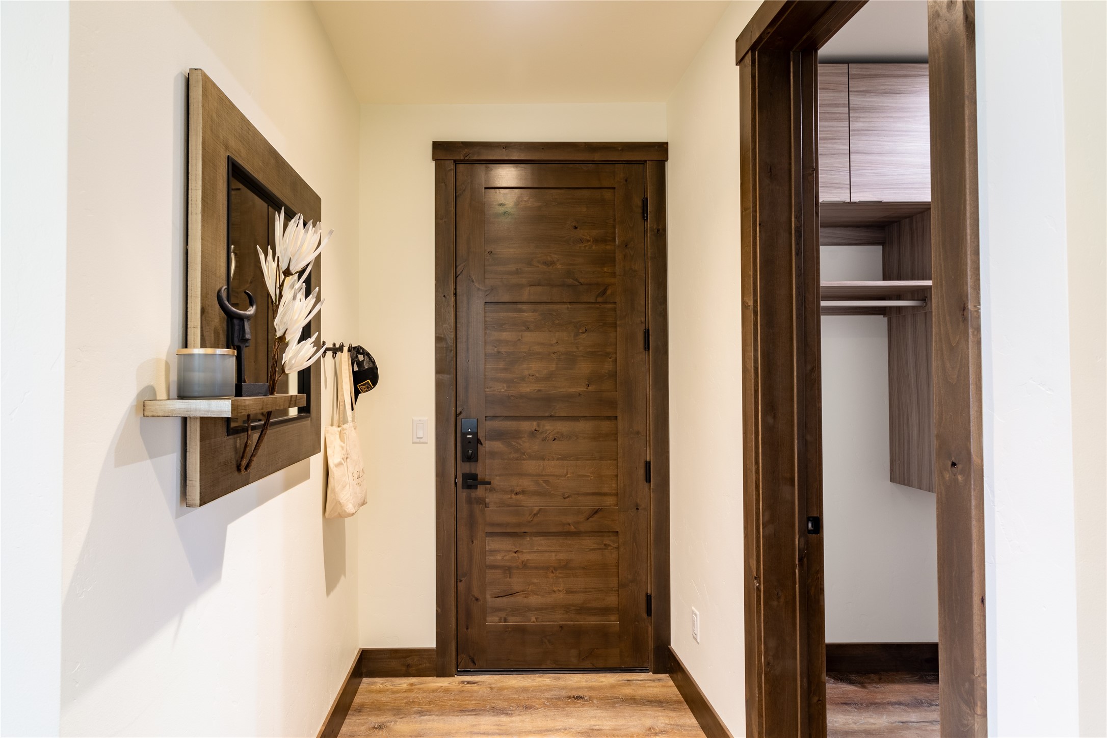 Entry hall with a dark wood paneled door, wood flooring, and an open built-in closet.