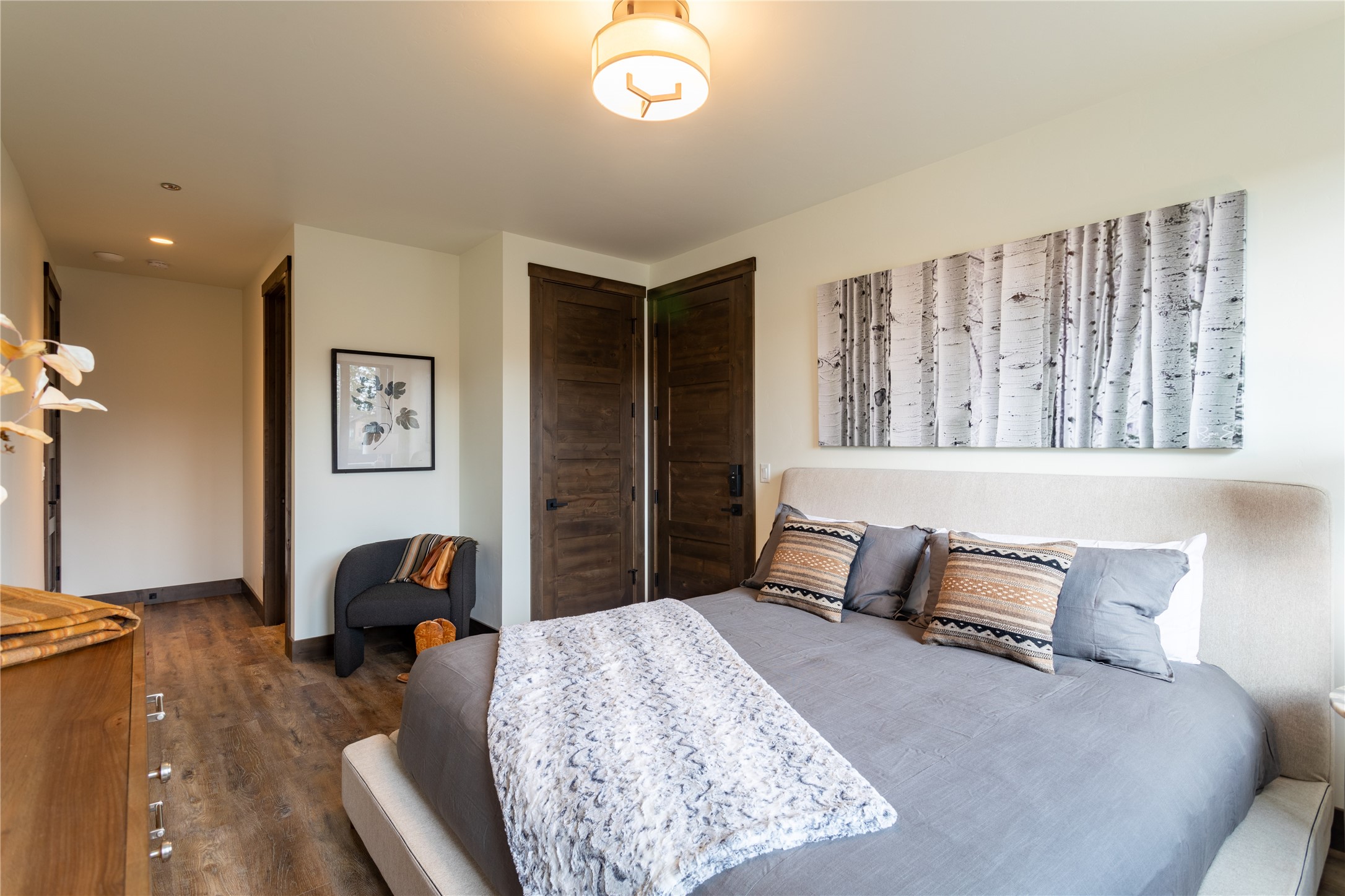 Bedroom with a gray bed, patterned pillows, dark wood doors, and birch-tree wall art.