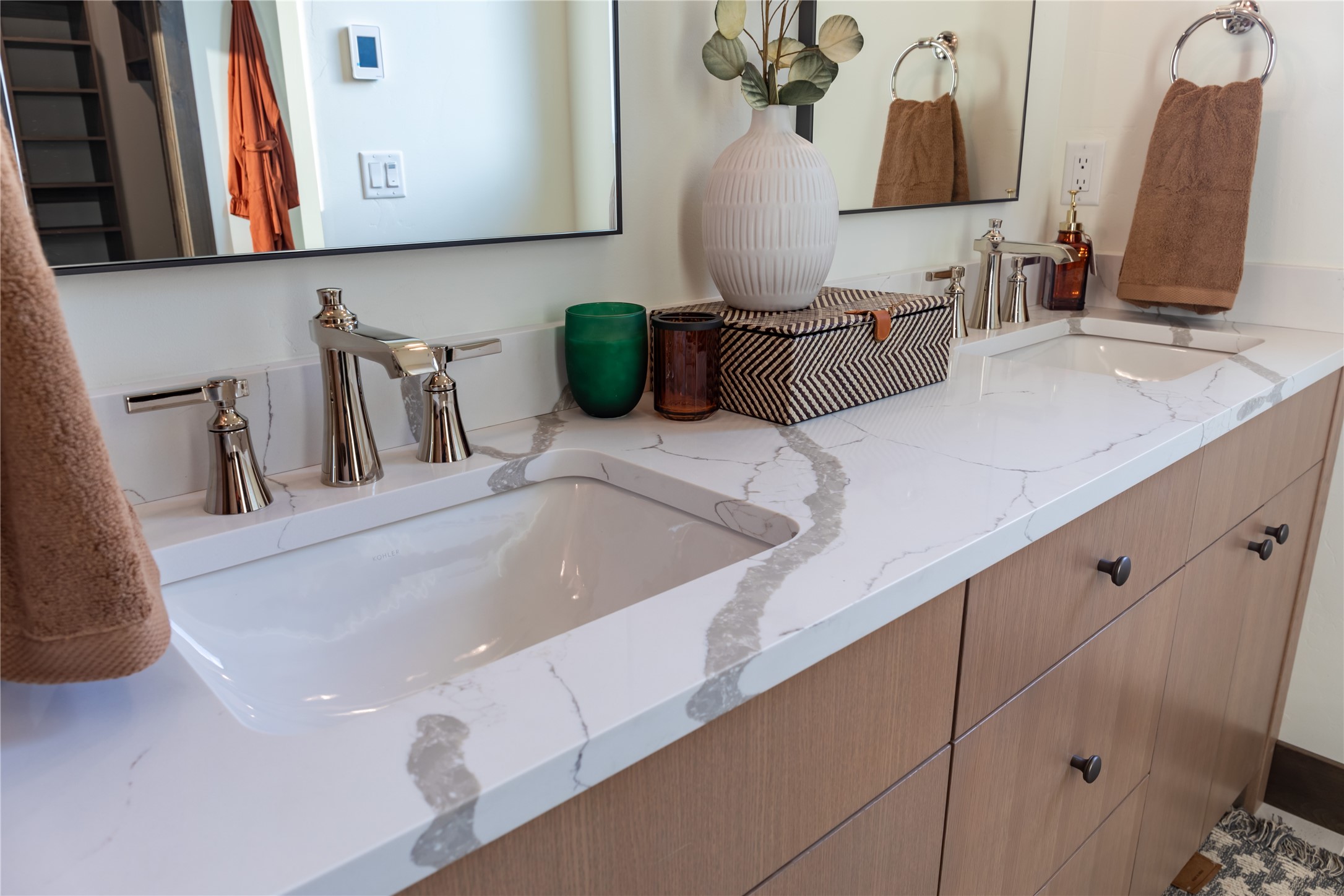 Bathroom vanity with two sinks, veined white countertop, wood cabinetry, and chrome fixtures.