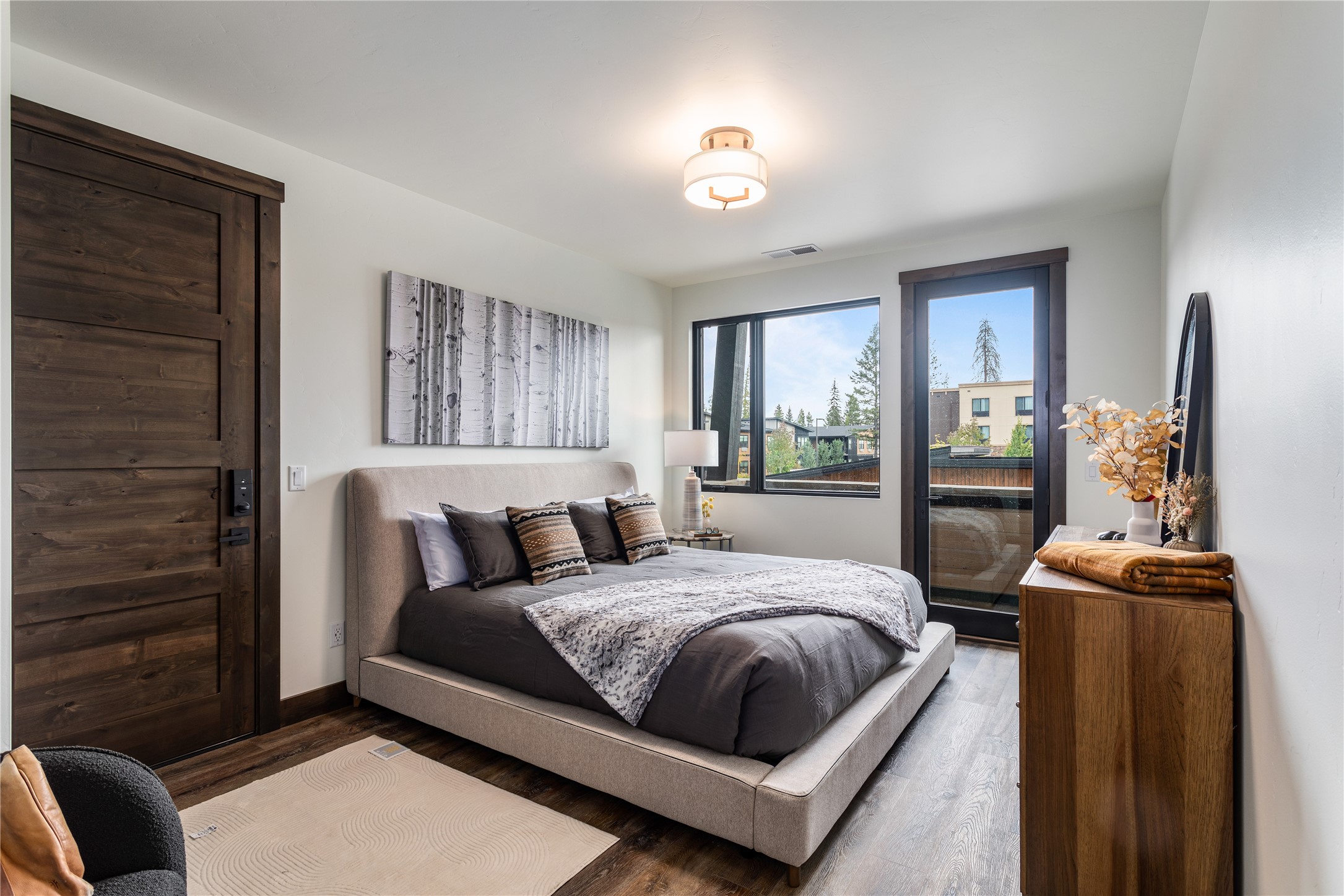 Staged bedroom with a large upholstered bed, dark wood barn door, and balcony access.