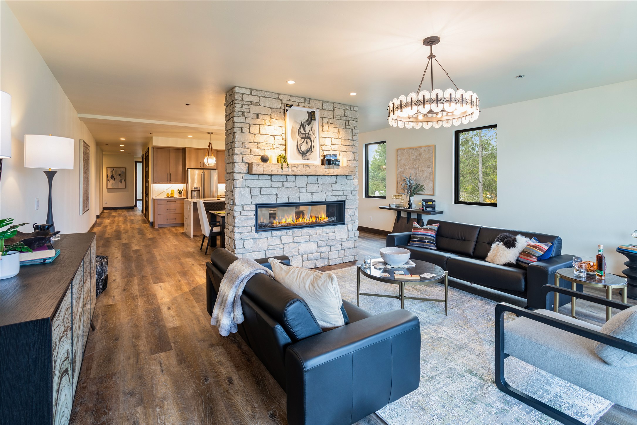 Open-plan living room with a stone fireplace, dark leather sofas, and a kitchen beyond.