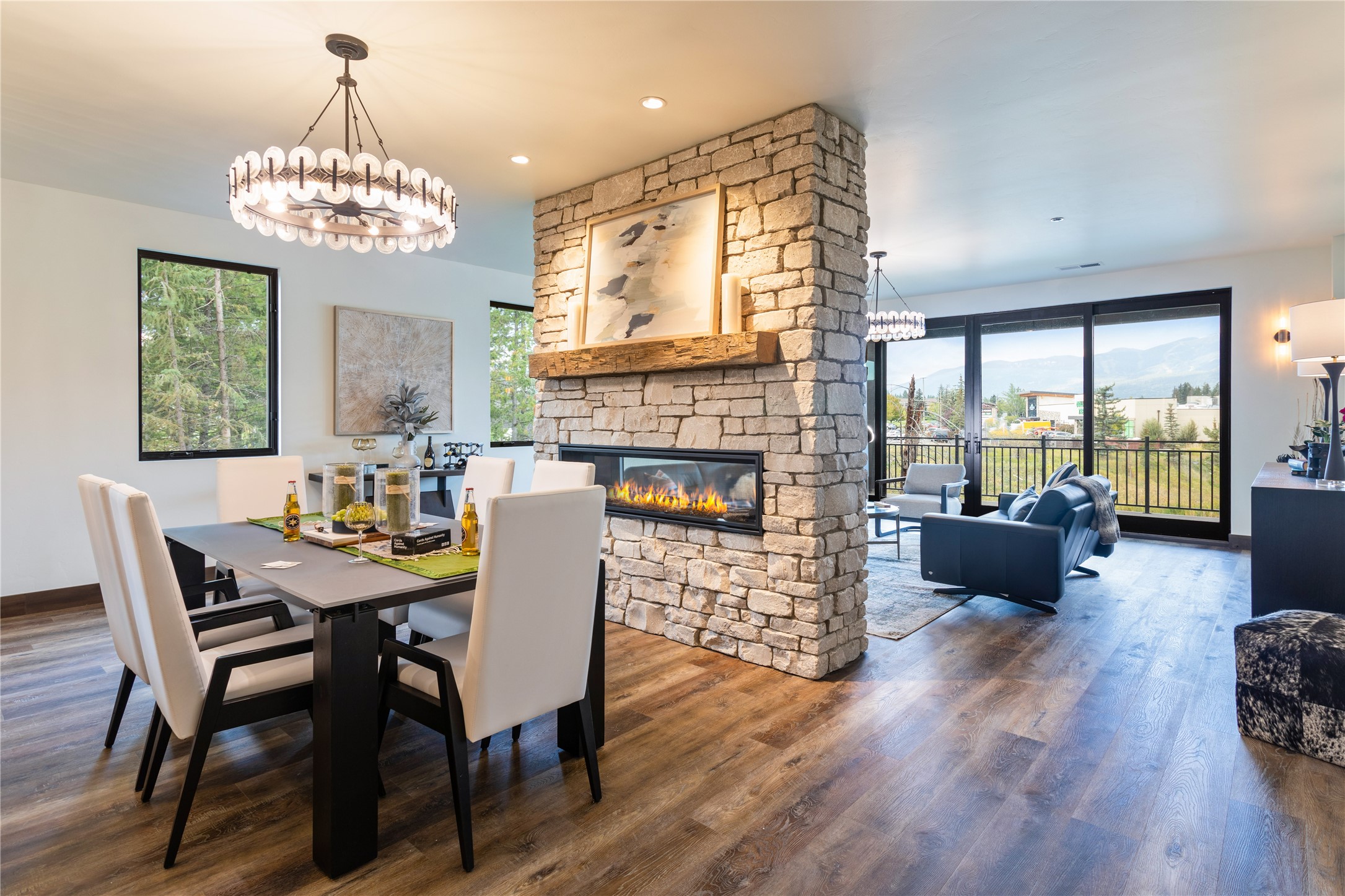 Open-plan dining and living room with a stone fireplace, blue sofa, and balcony doors framing mountain views.