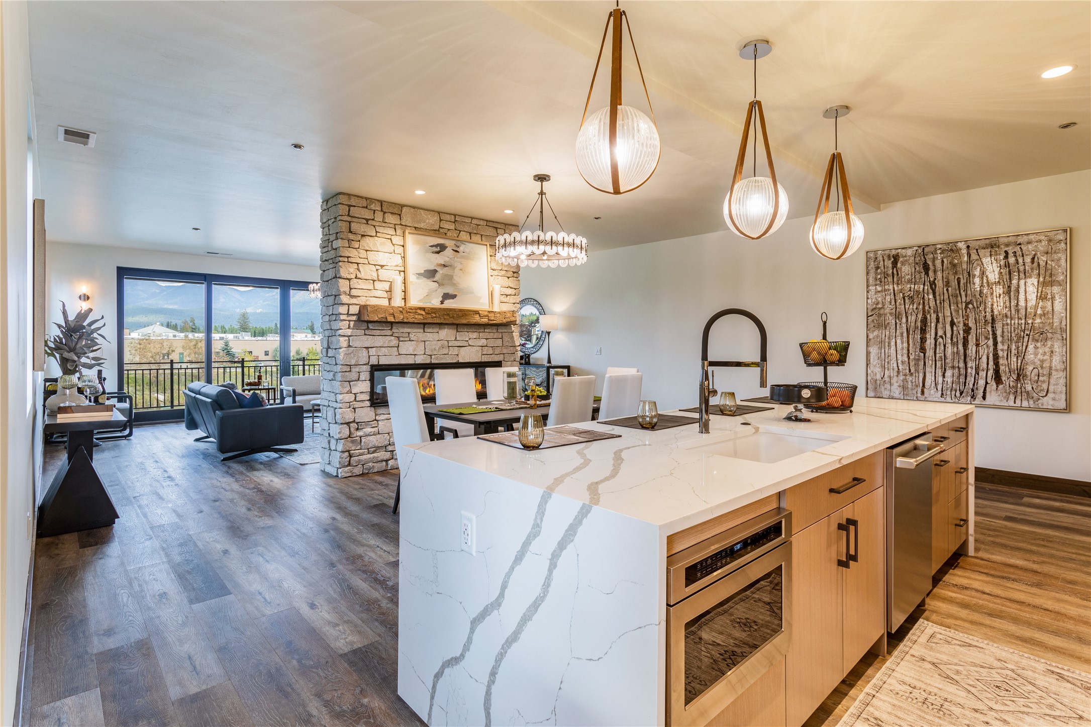 Open-plan kitchen and living area with a veined-stone island, stone fireplace, and mountain views.