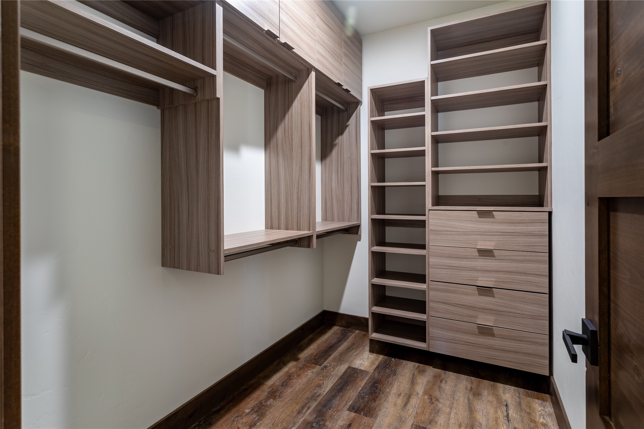Walk-in closet with custom wood shelving, hanging rods, built-in drawers, and hardwood flooring.