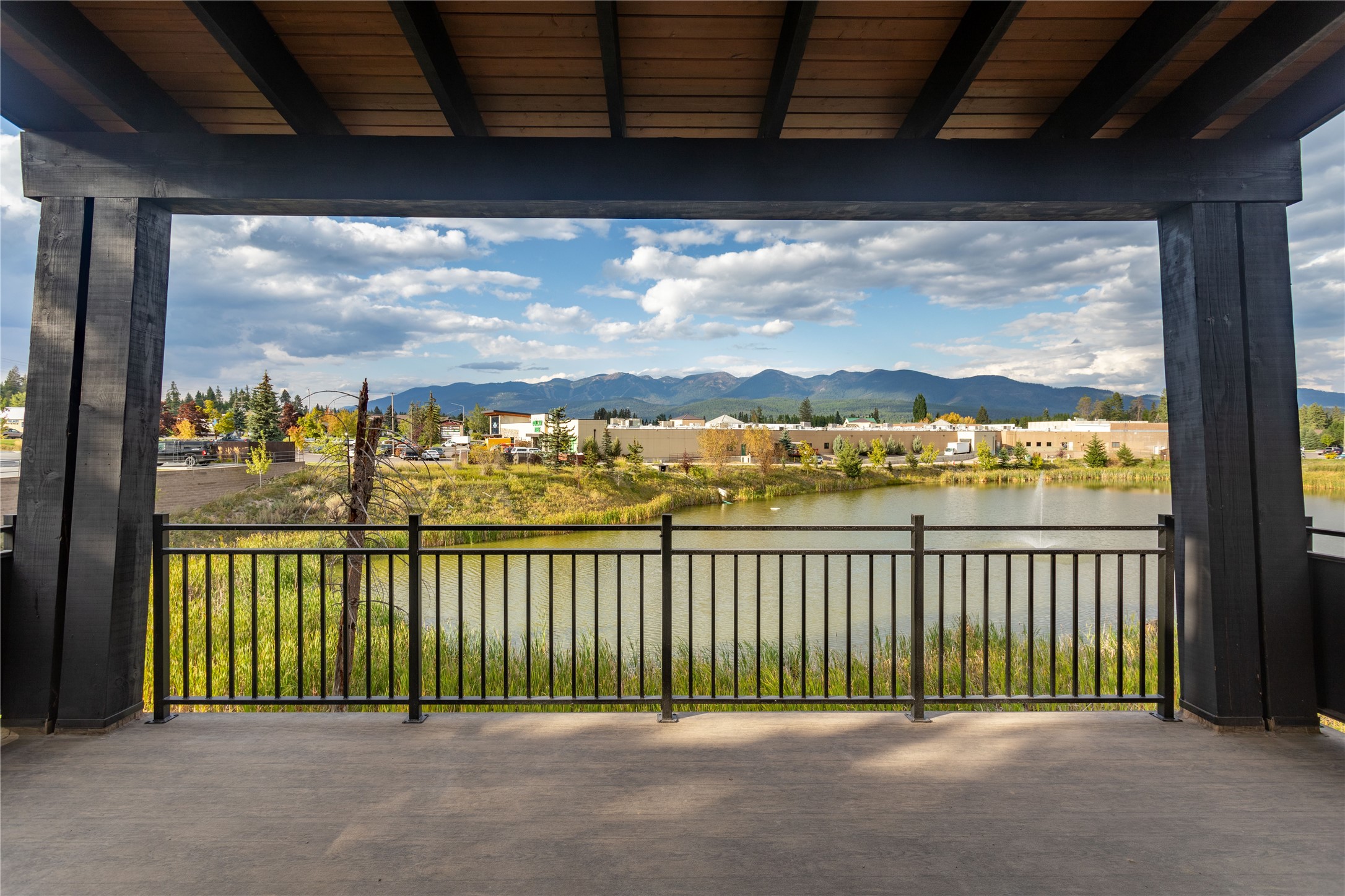 Covered patio overlooking a pond and distant mountains, framed by dark timber beams.