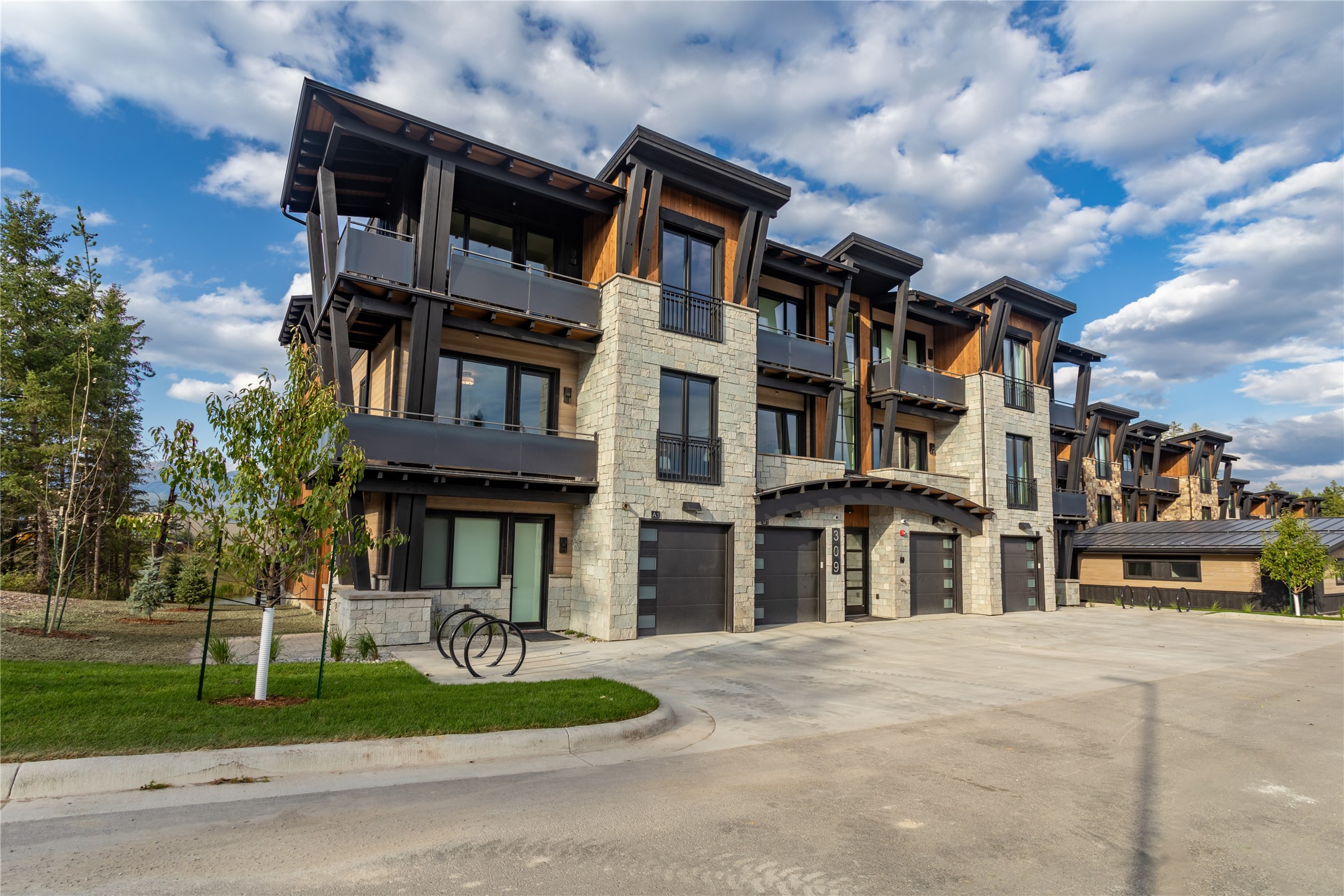 Modern stone and timber residential building with balconies and garage bays along a paved drive.