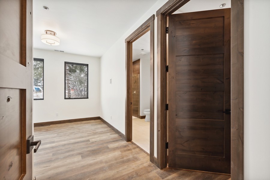 Vacant room with wood-look floors, two windows, and an open doorway to a bathroom.