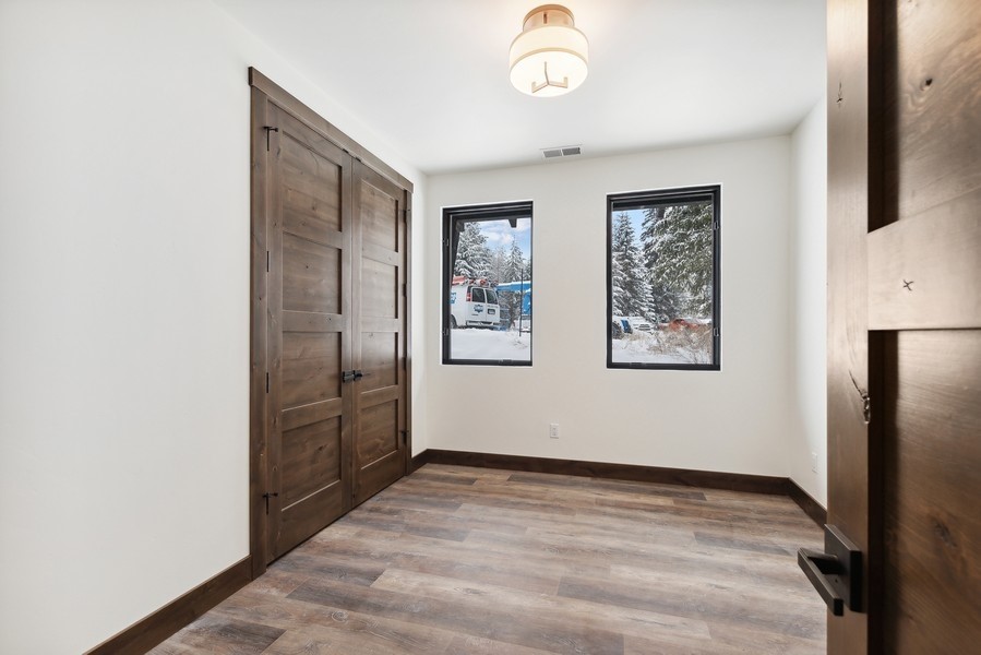 Small empty room with dark wood sliding barn doors and two windows overlooking snowy trees.