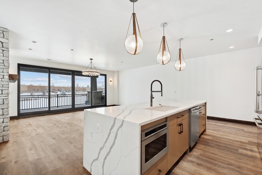 Kitchen with a veined quartz island, wood cabinetry, and sliding glass doors overlooking a snowy balcony.