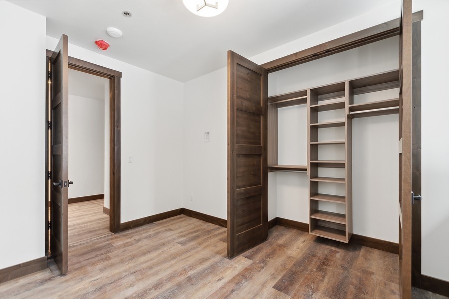 Walk-in closet with built-in dark wood shelves and hanging sections, viewed through open doors.