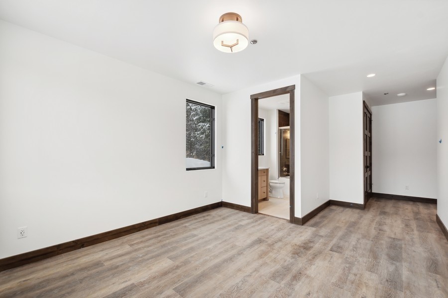Empty room with wood-look floors, dark trim, and a doorway to a bathroom.