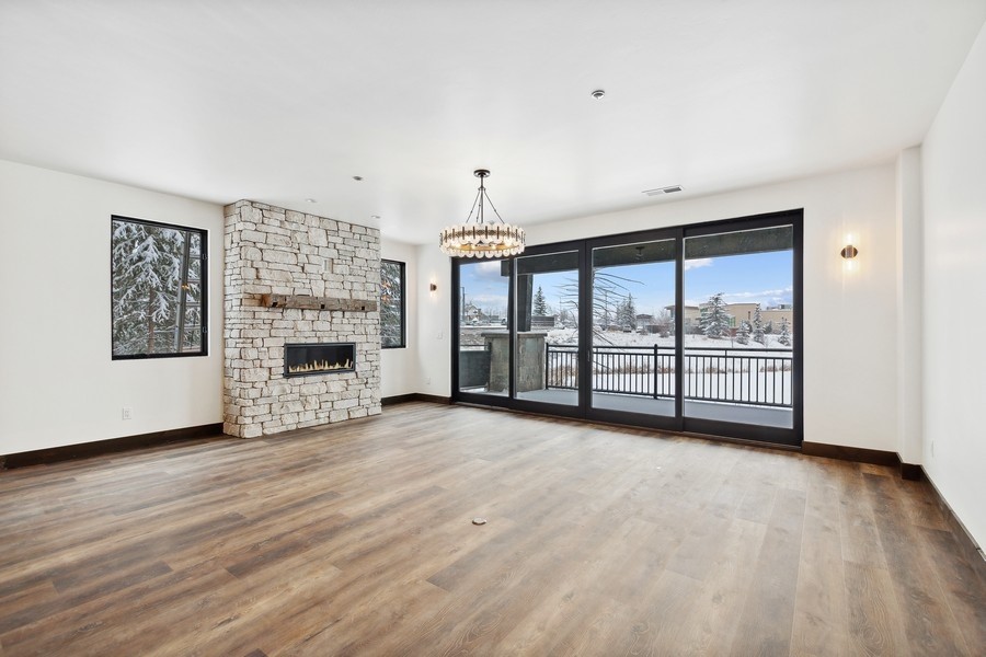 Empty living room with a stone fireplace and sliding glass doors overlooking a snowy balcony.